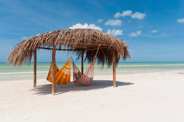 Fototapeta na wymiar A rustic hut with hammocks on a beach on Holbox Island in Mexico, in the background the blue sky and the Caribbean Ocean. Relaxation travel concept 