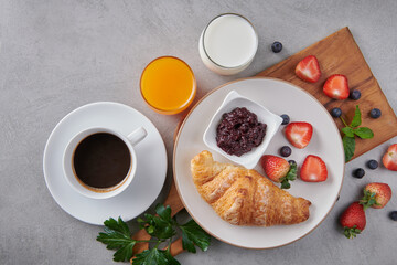 Different ingredients for breakfast. Continental breakfast with assortment of pastries, Croissants and strawberry Jam on plate on the wood board, coffees, milk and orange juice ,fresh strawberries.