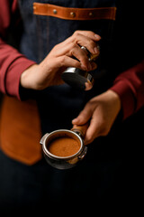 Woman barista holds in her hand portafilter with pressed ground coffee inside it.