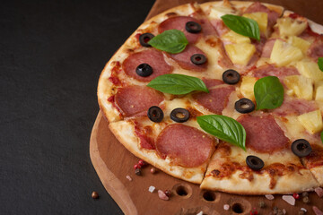 Italian pizza and pizza cooking ingredients on wooden pizza board. Dark stone background. Tomatoes on vine, mozzarella, black olives, herbs and spices. Mixture pizza Italian food. Copy Space. Top view