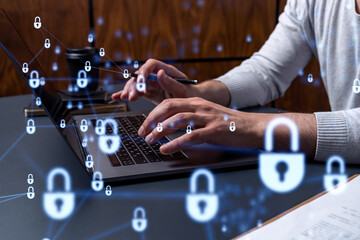 A programmer is typing a code on a keyboard to protect a cyber security from hacker attacks and save clients confidential data. Padlock Hologram icons over the typing hands.