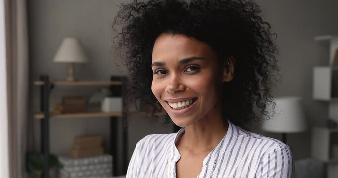 Head shot close up 35s African woman standing in living room daydreams look into distance. Female homeowner pose indoor looks at camera feels happy. Tenant, independent business lady portrait concept