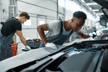 Two male mechanics inspects engine, car service