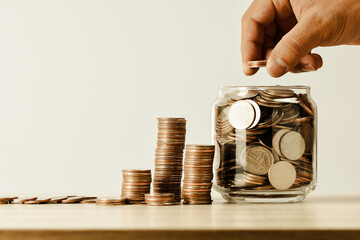 Thai coins are lined up and hand holding money in a jar on the table shown in the form of a graph...