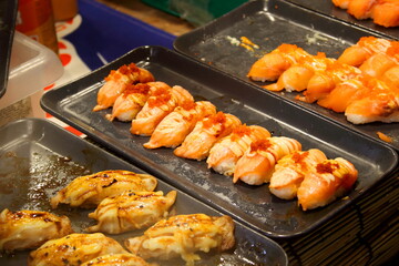 Sushi in row on black tray for sale, salmon grilled and mayonnaise on top in Thailand.