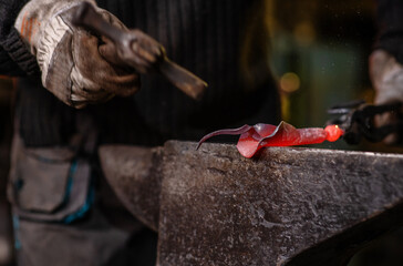A close-up image of a blacksmith's hands forging a jewelry flower from a hot sheet of metal. Manual rework in the forge concept