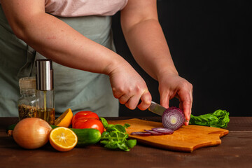 The chef cuts fresh vegetables on a wooden board. Cooking a burger.