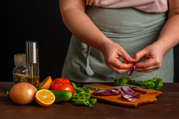 The chef cuts the red onion into rings on a wooden board. Cooking a burger.