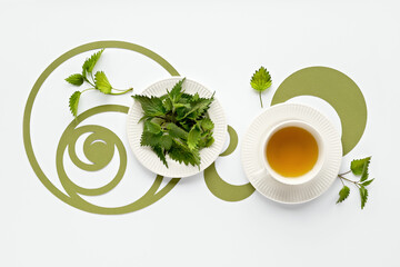 Nettle tea cup, stinging nettle herb leaves. Ornate flat lay, green paper Fibonacci sequence...