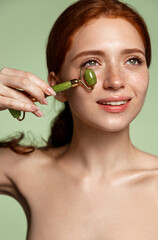 Vertical shot of beauty skincare model, redhead girl uses jade roller on healthy fresh glowing skin, self massage with tcm spa lifting tool for dark circles and puffiness, healthy beautiful face © Liubov Levytska