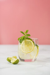 One glass with a drink - cucumber, ice cubes, mint and lime on a pink background