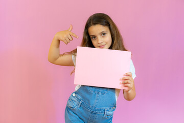 Smiling little girl holding empty pink board isolated over pink background.