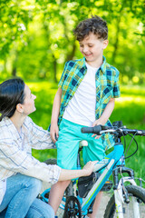 Obraz premium Mom helping her son learn to ride a bike in a summer park.