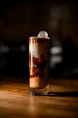 close-up of transparent glass with cold black coffee and milk on table