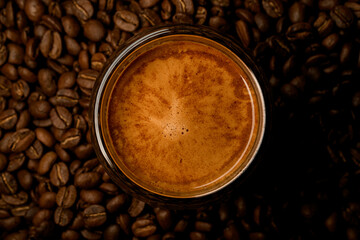 Close-up top view of round glass with foamy coffee drink on coffee beans background