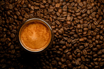 top view of glass with foamy coffee drink on coffee beans background