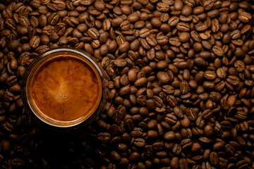beautiful top view of glass with foamy coffee drink on coffee beans background