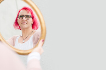 Junge Frau mit roten Haaren und Brille schaut durch einen Spiegel in die Ferne