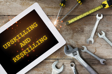 Upskilling and reskilling words on digital computer tablet and tools supplies on wooden background. New skills concept and technology transformation learning model idea