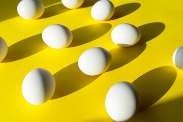 Many eggs on yellow surface, creativity picture with white  chicken egg, abstract composition with light and shadows