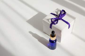 Bottle of essential oils, fluid collagen, serum in blue glass bottle with pipette near gift box with ribbon on white background. Beauty concept. Natural Organic Spa Cosmetic.