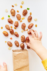 Explosion of dried fruits: dates from a paper bag close up on a white background. Creative concept of healthy snacks and healthy nutrition for children, close-up of a child's hands picking up dates