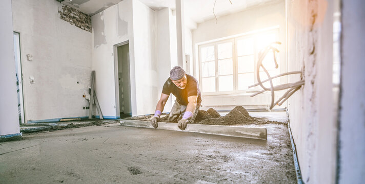 Filling the floor of a renovated apartment with concrete, screed and leveling the floor by construction workers. Even floors made of a mixture of cement, industrial concreting. Bright sun shine