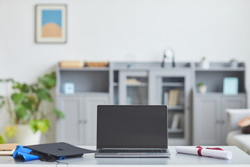 Background image of blank opened laptop screen with graduation hat on table