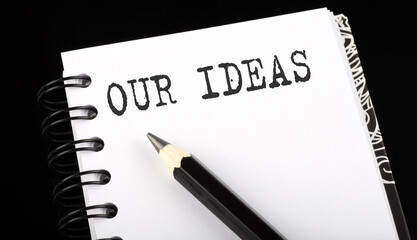 OUR IDEAS written text in small notebook on a black background