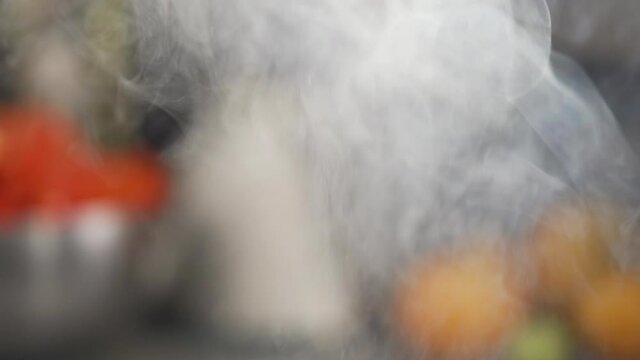 Steam rising from a pot or pan in slow motion while cooking. Kitchen out of focus behind the steam.