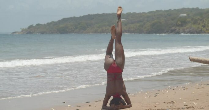 A contortionist in a hand stand position before dismounting into a pose with waves crashing the shoreline in the background