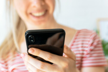 Happy young woman looks into the phone and smiling. Focus on the smartphone. A blond hair girl...