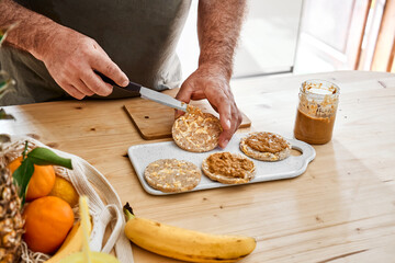 Man preparing healthy organic breakfast with puffed corn cakes, peanut butter and banana. Natural protein diet and healthy eating concept.