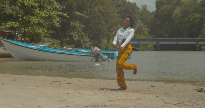Choreography afro dance moves from a young African woman at a river location with boats anchored in the background