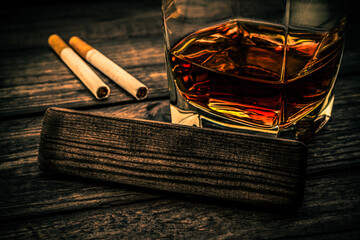 Glass of brandy with cigarettes and the empty wooden plank on an old wooden table. Close up view, focus on the wooden plank