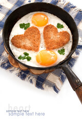 Fried eggs with slices of bread in the shape of a heart in the frying pan