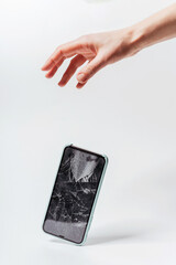 Smartphone falling out of hand on a white background. Crash protective tempered glass for smartphone. Smartphone with broken screen falls out of hand