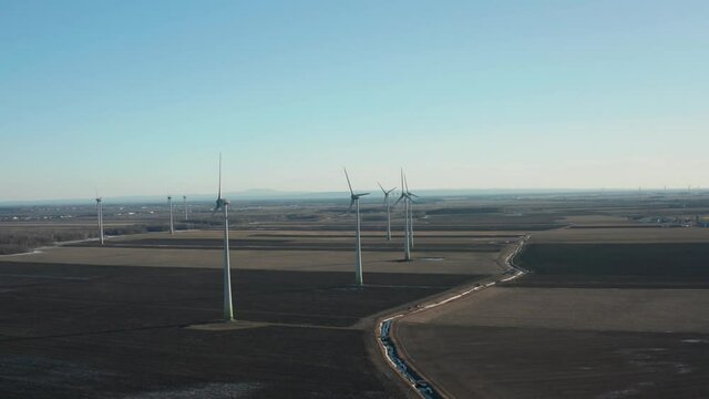drone going around a wind farm turbines looking the front of the turbines in a sunny day