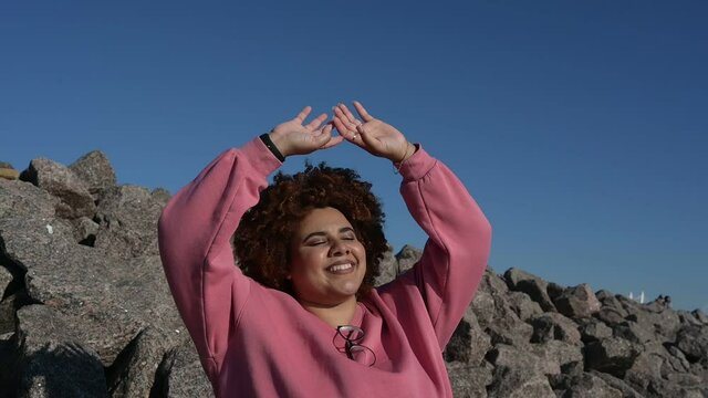 Beautiful happy smiling plus size African black woman afro hair in pink hoody outdoor enjoying bright sunny weather and blue sky. Body imperfection, acceptance body positive diversity concept.