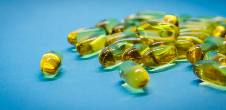 Fish oil capsules with omega 3 and vitamin D, isolated on blue background. Yellow vitamin pills. Medicine and healthy.