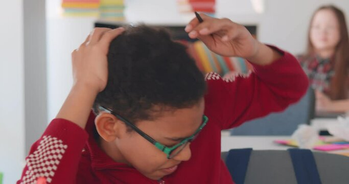 Angry school bully throwing paper ball at new african boy sitting at desk in classroom