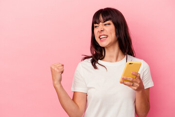 Young caucasian woman holding a mobile phone isolated on pink background raising fist after a victory, winner concept.