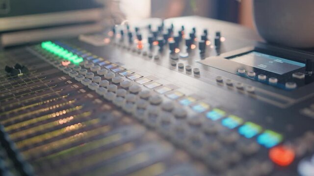 Professional audio recording mixing console with faders and illuminated knobs and buttons and an lcd screen during a recording session. Smooth pan sliding shot in 4K; Shallow depth of Field.