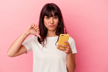 Young caucasian woman holding a mobile phone isolated on pink background showing a dislike gesture, thumbs down. Disagreement concept.