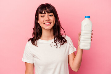 Young caucasian woman holding a bottle of milk isolated on pink background happy, smiling and cheerful.