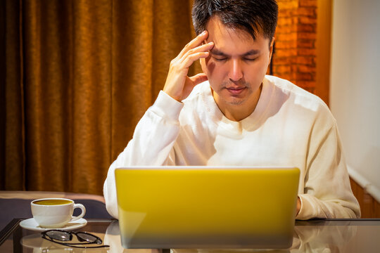 headache, tense young asian man working on laptop computer in bedroom at night
