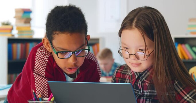 Two preteen diverse students using laptop in classroom