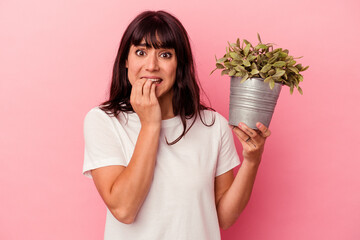 Young caucasian woman holding a plant isolated on pink background biting fingernails, nervous and...
