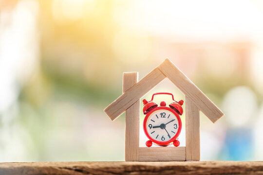 Home model and alarm clock put on the wood on sunlight in the public park, for buying or installment with real estate concept.