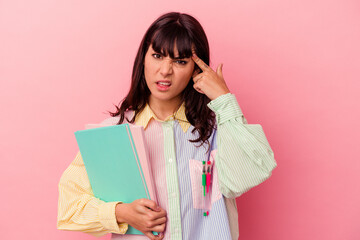 Young student caucasian woman holding books isolated on pink background showing a disappointment gesture with forefinger.